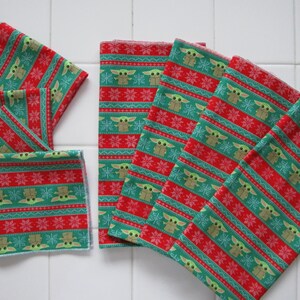 Puede incluir: Varios art&iacute;culos de tela estampada en verde, rojo y blanco. El patr&oacute;n presenta un dise&ntilde;o repetitivo de un personaje, copos de nieve y rayas. Los art&iacute;culos parecen ser servilletas de tela o textiles similares.