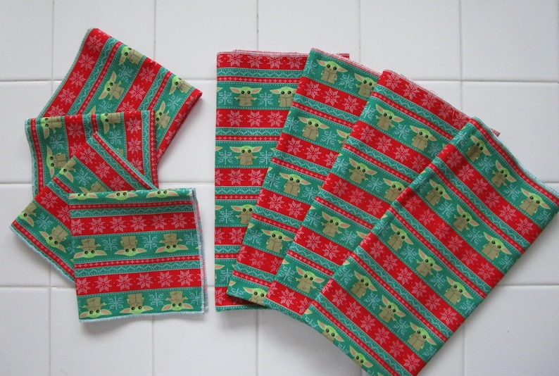 Puede incluir: Varios art&iacute;culos de tela estampada en verde, rojo y blanco. El patr&oacute;n presenta un dise&ntilde;o repetitivo de un personaje, copos de nieve y rayas. Los art&iacute;culos parecen ser servilletas de tela o textiles similares.