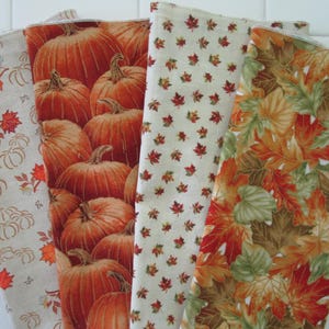May include: A collection of five fall-themed fabric napkins. The napkins feature various patterns, including pumpkins, maple leaves, and floral designs in shades of orange, brown, and cream. Perfect for autumn decor.