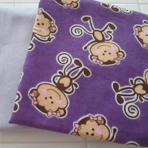 May include: Two pieces of fabric. One is a solid light lavender color. The other is a deep purple with a repeating pattern of cartoon monkeys with brown faces, pink bows, and white outlines.