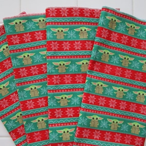 Puede incluir: Cuatro pa&ntilde;os de tela estampados en verde, rojo y blanco. El patr&oacute;n presenta un dise&ntilde;o repetitivo de un personaje de una popular serie de ciencia ficci&oacute;n, copos de nieve y rayas horizontales. Los pa&ntilde;os son probablemente pa&ntilde;os de cocina o similares.