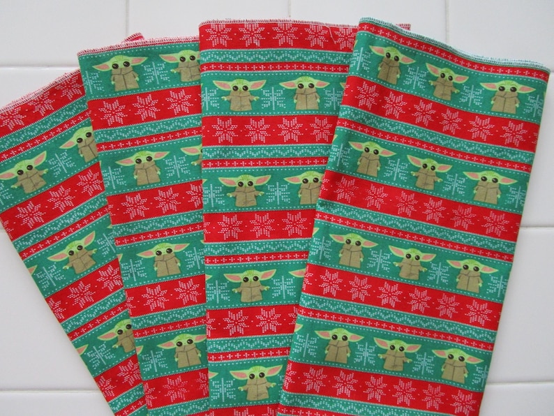 Puede incluir: Cuatro pa&ntilde;os de tela estampados en verde, rojo y blanco. El patr&oacute;n presenta un dise&ntilde;o repetitivo de un personaje de una popular serie de ciencia ficci&oacute;n, copos de nieve y rayas horizontales. Los pa&ntilde;os son probablemente pa&ntilde;os de cocina o similares.