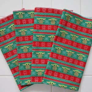 Puede incluir: Cuatro pa&ntilde;os de tela doblados, rojos y verdes. Los pa&ntilde;os tienen un patr&oacute;n repetitivo de un personaje de una popular serie de ciencia ficci&oacute;n, copos de nieve y rayas. Probablemente se trate de pa&ntilde;os de cocina o servilletas.