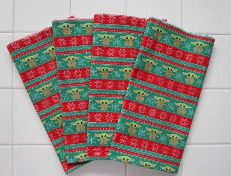 Puede incluir: Cuatro pa&ntilde;os de tela doblados, rojos y verdes. Los pa&ntilde;os tienen un patr&oacute;n repetitivo de un personaje de una popular serie de ciencia ficci&oacute;n, copos de nieve y rayas. Probablemente se trate de pa&ntilde;os de cocina o servilletas.