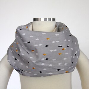 Könnte beinhalten: Grauer Stoff-Lätzchen mit geometrischem Muster aus schwarzen und gelben Rauten. Das Lätzchen hat den Schriftzug "bib" unten.