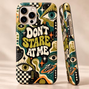 May include: A phone case featuring the text DON'T STARE AT ME in white, surrounded by a dark green, black, and orange pattern of eyes, stars, planets, and checkered squares. The design covers the back and side of the phone case.