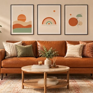 May include: A cognac leather sofa with various throw pillows, a round marble coffee table, and a yellow ottoman. Three framed wall art prints feature abstract sun and rainbow motifs. A large potted plant stands to the left of the sofa.