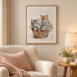 May include: A framed wall art print featuring a painting of three kittens sitting inside a woven wicker basket. One kitten is orange tabby, while the other two are gray tabby, all nestled among soft fabric scraps with pink ribbons.