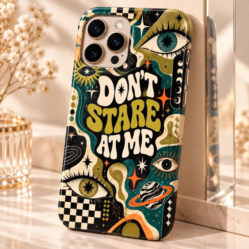 May include: A smartphone case featuring a dark teal, olive green, and orange graphic design with the text "DON'T STARE AT ME" in a bold, wavy font. The pattern includes multiple stylized eyes, stars, a planet with rings, and a black and white checkerboard.