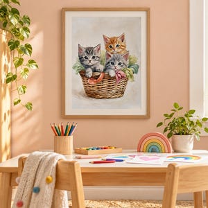 May include: A framed wall art print featuring three kittens, one orange tabby and two grey tabby, sitting inside a woven wicker basket. The kittens are surrounded by soft green fabric and pink ribbons, rendered in a painterly style with a light background.