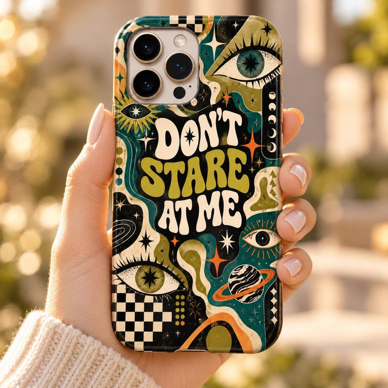 May include: A phone case featuring a psychedelic design with the text "DON'T STARE AT ME" in a wavy font. The artwork includes multiple eyes, stars, a planet with rings, and a black and white checkerboard pattern in shades of green, orange, and black.