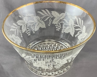 Könnte beinhalten: Eine klare Glasschale mit goldfarbenem Rand und einem geätzten Design aus Weinblättern und Trauben an der Außenseite. Der Boden der Schale weist ein strukturiertes Rautenmuster auf, das einen Kontrast zu den glatten oberen Wänden bildet.