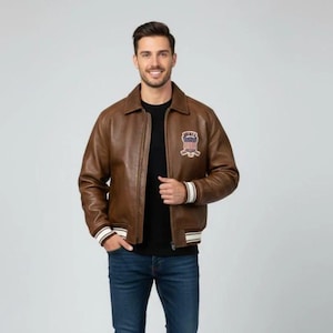 May include: A brown leather bomber jacket featuring a classic collar, a front zipper closure, and ribbed cuffs with white stripes. A patch with red, white, and blue colors and the text "SWIRE" is displayed on the left chest area.