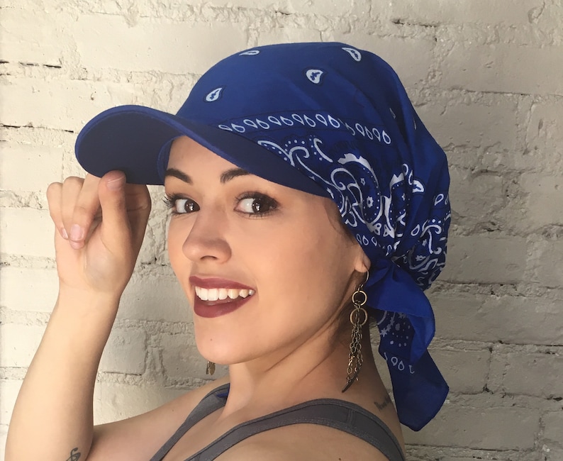 May include: A blue bandana tied around the head as a hat with a blue baseball cap on top. The cap has a curved brim and is worn backwards.