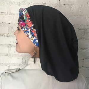 K&ouml;nnte beinhalten: Eine schwarze Kopfbedeckung mit buntem Muster und langem, flie&szlig;endem Design. Die Kopfbedeckung ist aus weichem, dehnbarem Stoff.