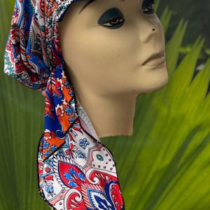 May include: A blue visor hat with a colorful paisley print fabric attached. The fabric features red, orange, blue, and white patterns. The hat is displayed on a mannequin head against a green background.