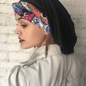 K&ouml;nnte beinhalten: Ein schwarzer und bunt gemusterter Turban mit einer schwarzen Satin-Au&szlig;enschicht. Der Turban wird auf dem Kopf einer Person getragen.
