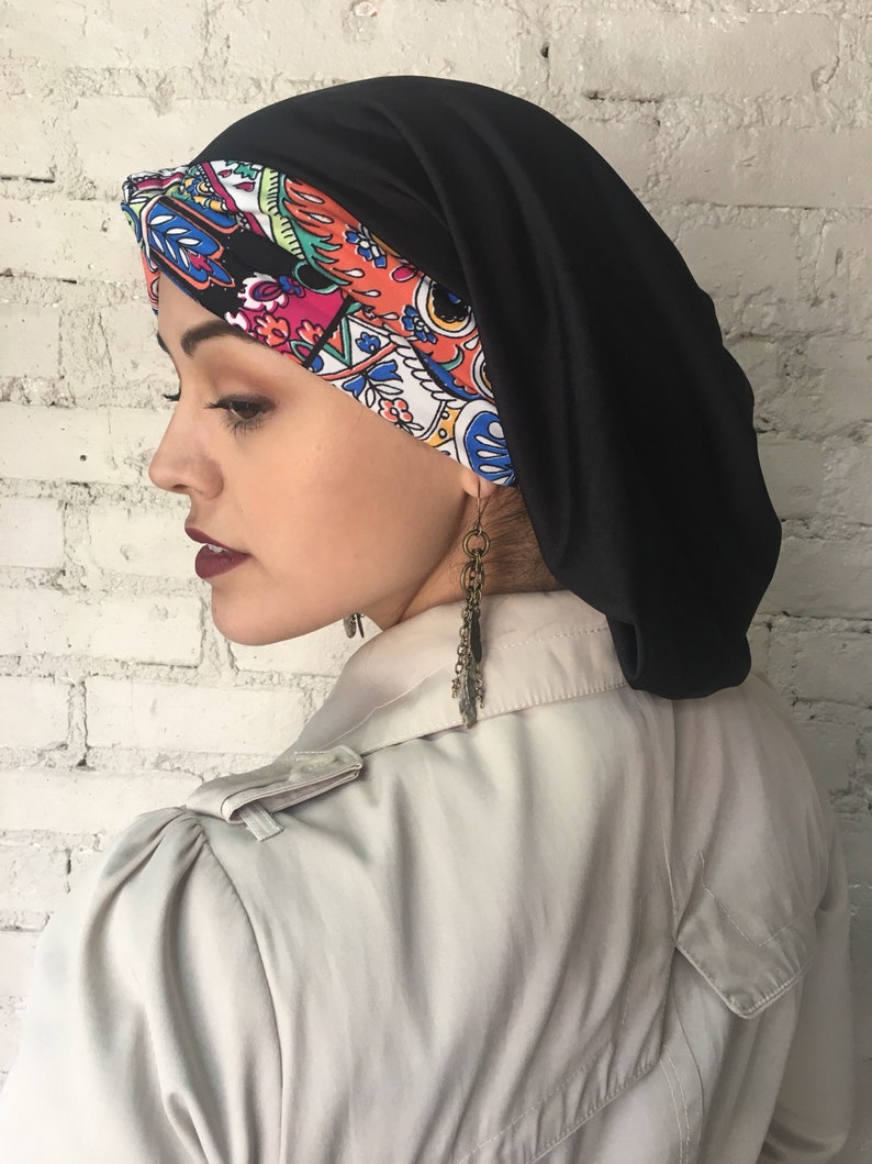 K&ouml;nnte beinhalten: Ein schwarzer und bunt gemusterter Turban mit einer schwarzen Satin-Au&szlig;enschicht. Der Turban wird auf dem Kopf einer Person getragen.