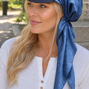 Puede incluir: Un cubrecabezas azul con visera azul marino sólida y una tela azul texturizada que se ata a un lado. Este accesorio combina la estructura de una gorra de béisbol con el estilo suave y drapeado de un pañuelo, creando una pieza versátil.