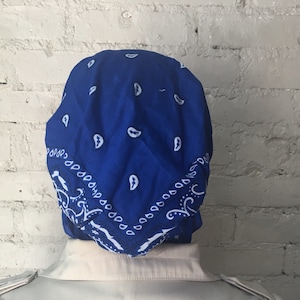 May include: A blue bandana with a white paisley pattern. The bandana is folded and tied on a person's head.