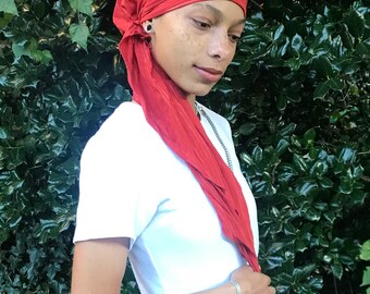 Op de afbeelding: Een persoon draagt ​​een rode gestreepte hoofddoek met een wit T-shirt en een zwarte broek.