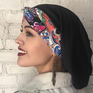 K&ouml;nnte beinhalten: Eine schwarze Satin-Schlafhaube mit einem bunten Paisley-Muster auf der Vorderseite. Die Haube wird auf dem Kopf einer Person getragen.
