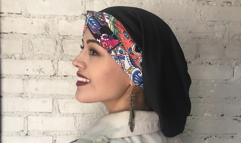 K&ouml;nnte beinhalten: Eine schwarze Satin-Schlafhaube mit einem bunten Paisley-Muster auf der Vorderseite. Die Haube wird auf dem Kopf einer Person getragen.