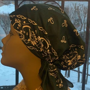 May include: A dark green bandana-style head covering with a white paisley pattern. The head covering is tied at the back and is displayed on a mannequin head. The mannequin is wearing a gold sequined top.