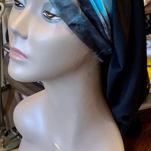 Può includere: Un turbante nero e blu con un motivo tie-dye. Il turbante è su una testa di manichino con il testo "HARLEM 125" sul petto.