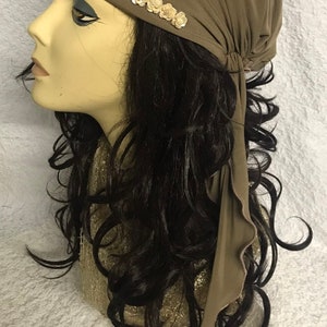 May include: A brown fabric head wrap with a row of white embellishments. The wrap is tied at the back of the head and has a long tail that hangs down the back.