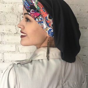 K&ouml;nnte beinhalten: Ein schwarzer und farbenfroher Turban-Kopfbedeckung mit Muster. Die Kopfbedeckung besteht aus einem weichen, dehnbaren Stoff. Der Stoff ist au&szlig;en schwarz und innen mit einem farbenfrohen Paisley-Muster versehen.