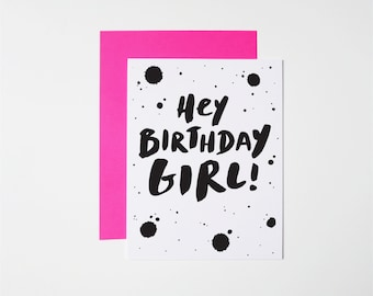 May include: A white card with black ink splatter and the text "Hey Birthday Girl!" in bold black lettering. The card has a pink envelope.