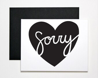 May include: A white card with a black heart shape and the word "sorry" written in white cursive inside the heart.