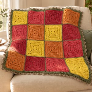Könnte beinhalten: Eine quadratische Häkeldecke mit einem Gitter aus sechzehn Granny Squares in abwechselnden Gelb-, Orange- und Rottönen. Die Decke ist mit einem dunkel olivgrünen Garnrand eingefasst, der einen kleinen, gewellten und strukturierten Abschluss bildet.
