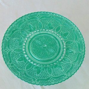 May include: A green glass plate with a raised, embossed design of leaves and dots. The plate has a scalloped edge.