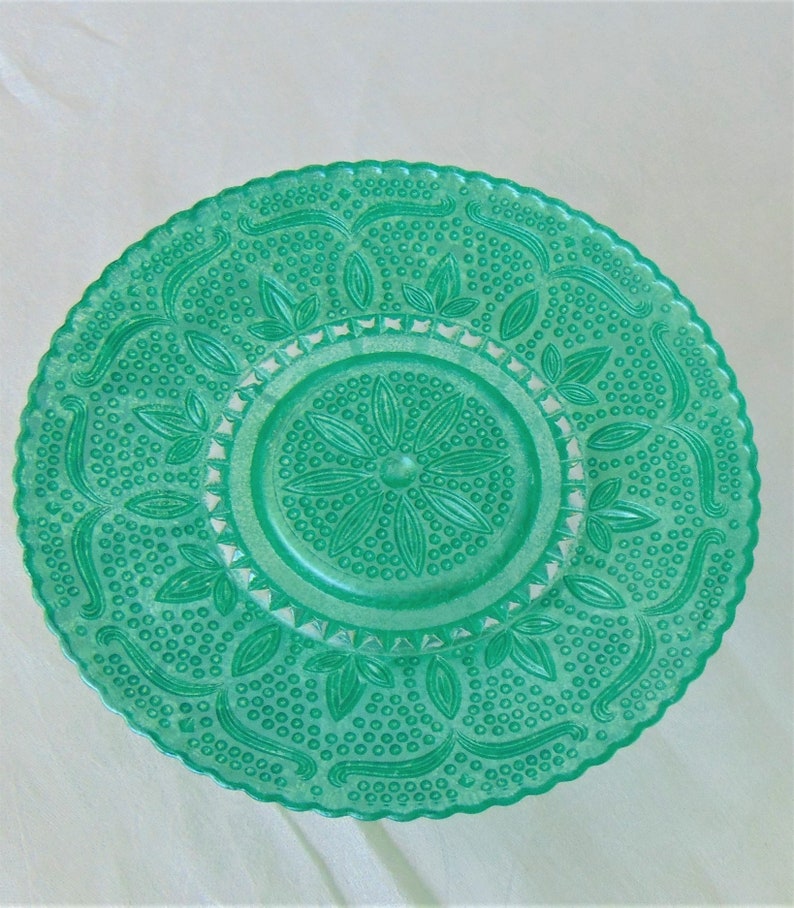 May include: A green glass plate with a raised, embossed design of leaves and dots. The plate has a scalloped edge.