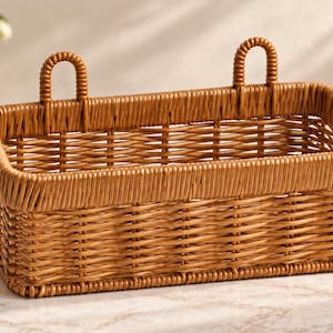 May include: A rectangular brown woven basket with a structured rim and two integrated vertical loops on the back edge for hanging. The basket features a consistent, tight weave pattern throughout its sides and base, constructed from a smooth material.
