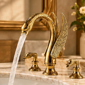 May include: A gold-toned bathroom faucet shaped like a swan with detailed wing textures on the spout. The faucet features two separate handles, each topped with a small swan head design, and water flows from the main swan head spout.