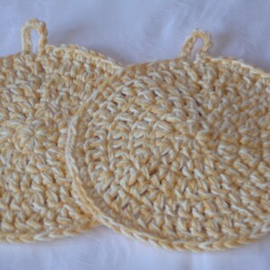 May include: Two crocheted pot holders in a yellow and white color scheme. The pot holders have a loop handle for easy grabbing.