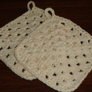 May include: Two crocheted pot holders in a light cream color. The pot holders are square shaped with a loop at the top for hanging.