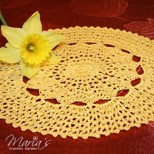May include: A yellow crocheted doily with a delicate floral pattern. The doily is on a red background with a yellow daffodil flower.