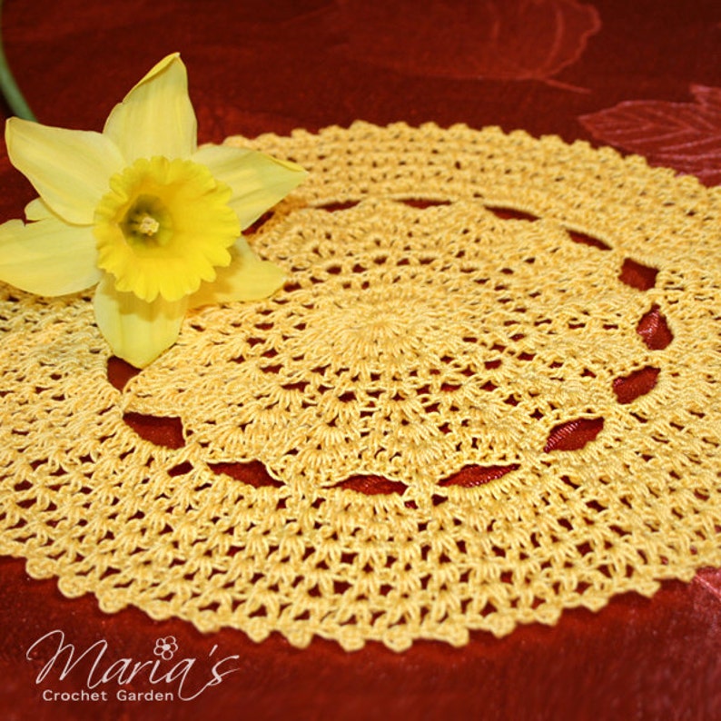 May include: A yellow crocheted doily with a delicate floral pattern. The doily is on a red background with a yellow daffodil flower.