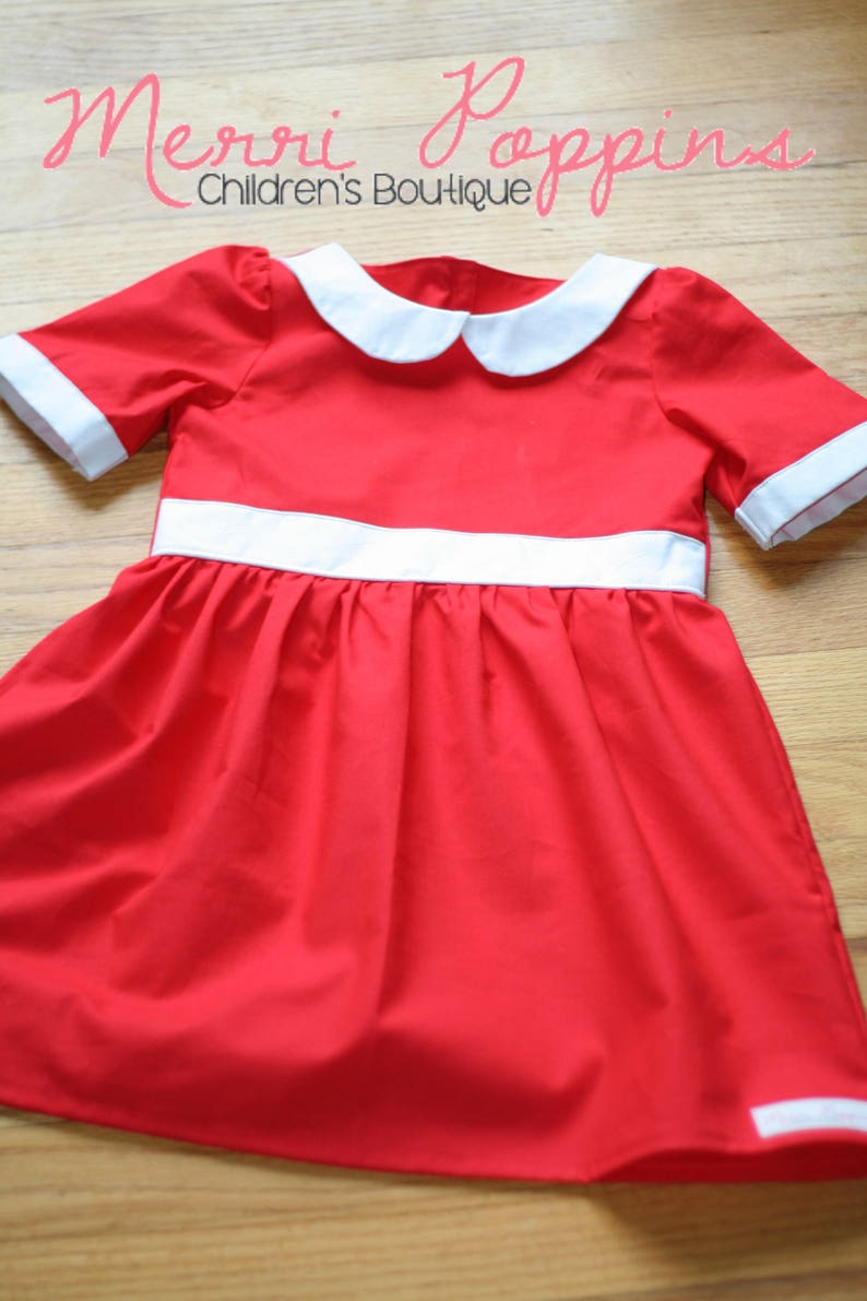 Op de afbeelding: Een rode jurk met een witte kraag en een witte bies rond de taille. De jurk heeft korte mouwen en een geplooide rok. De jurk ligt op een houten oppervlak. De tekst "Merri Pppins Children's Boutique" is zichtbaar bovenaan de afbeelding.