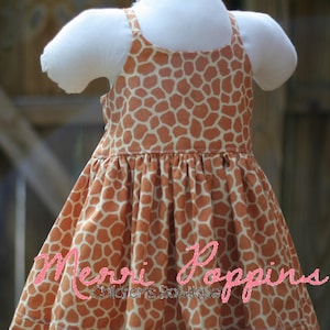 K&ouml;nnte beinhalten: Ein &auml;rmelloses Kleid mit Giraffenmuster in Braun- und Wei&szlig;t&ouml;nen. Das Kleid hat einen gerafften Rock und einen schlichten Oberteil. Das Kleid ist mit "Merri Poppins Children's Boutique" beschriftet.