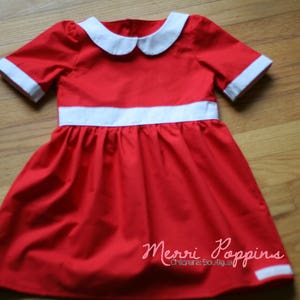 Op de afbeelding: Een rode jurk met een witte kraag en witte bies rond de taille. De jurk heeft een geplooide rok en is gelabeld "Merri Poppins Children's Boutique."