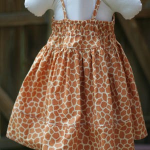K&ouml;nnte beinhalten: Ein &auml;rmelloses Kleid mit Giraffenmuster. Das Kleid hat eine geraffte Taille und einen Stufenrock. Das Kleid ist aus einem weichen, leichten Stoff.