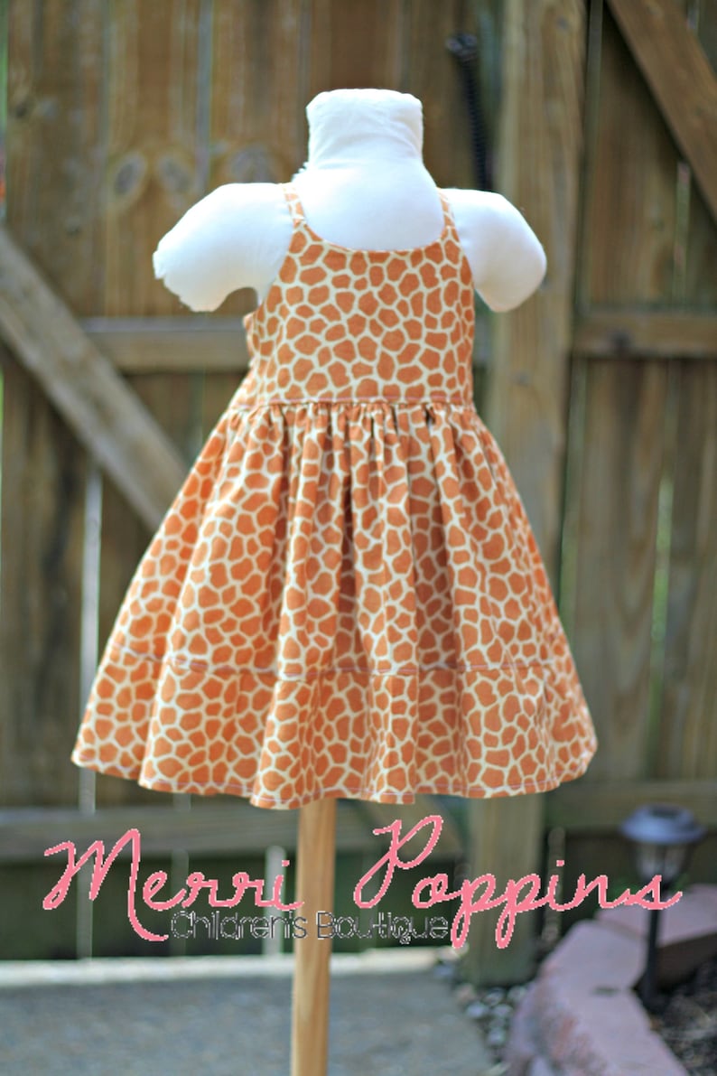 K&ouml;nnte beinhalten: Ein &auml;rmelloses Kleid mit Giraffenmuster. Das Kleid ist auf einer Holzpuppe und hat einen gerafften Rock. Das Kleid ist orange und wei&szlig;.