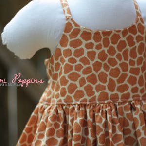 K&ouml;nnte beinhalten: Ein &auml;rmelloses Kleid mit Giraffenmuster. Das Kleid hat einen gerafften Rock und einen wei&szlig;en Oberteil.