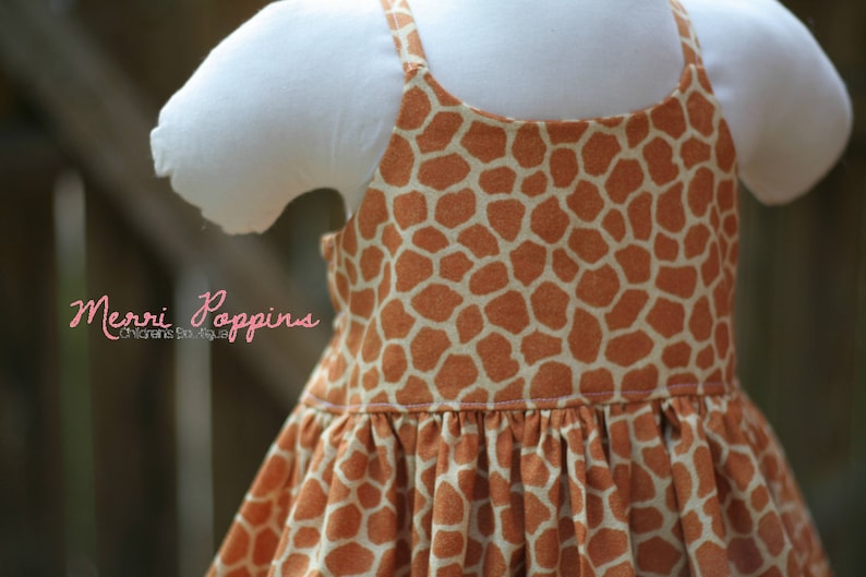 K&ouml;nnte beinhalten: Ein &auml;rmelloses Kleid mit Giraffenmuster. Das Kleid hat einen gerafften Rock und einen wei&szlig;en Oberteil.