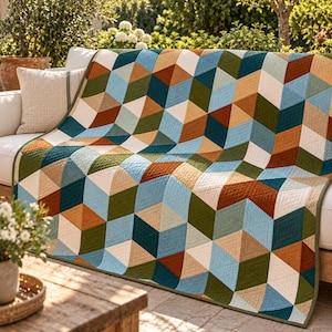 May include: A quilted blanket featuring a geometric pattern of repeating cubes in shades of teal, olive green, rust orange, light blue, and cream. The fabric has a visible stitched texture throughout, creating a structured, multi-colored diamond design.